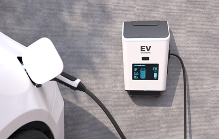 White electric car plugged into a wall-mounted EV charging station with a digital display